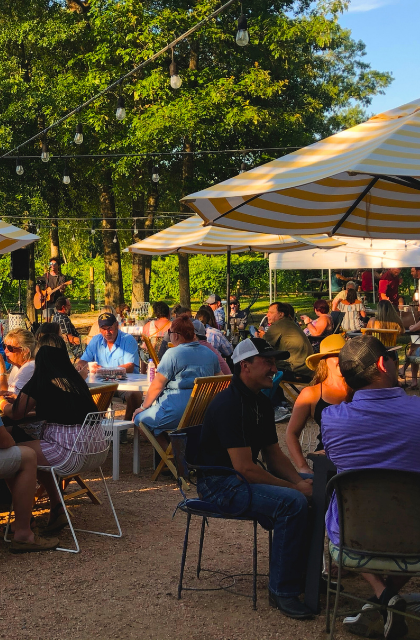 Outdoor dining area with string lights, umbrellas, and live music, creating a vibrant and inviting atmosphere for visitors.