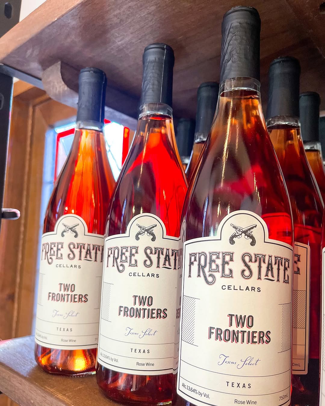 Bottles of Free State Cellars Two Frontiers Rose Wine displayed on a wooden shelf.